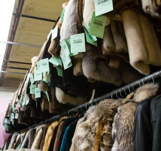 Rows of fur coats with green inventory tags on storage racks
