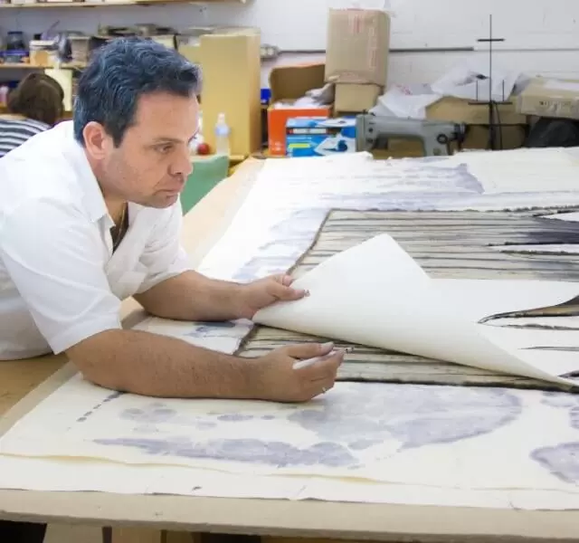 Furrier at a work table laying a paper pattern over fur pelts
