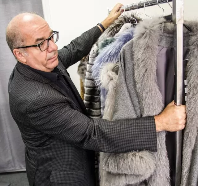 Furrier inspecting light grey fur coats on a rack