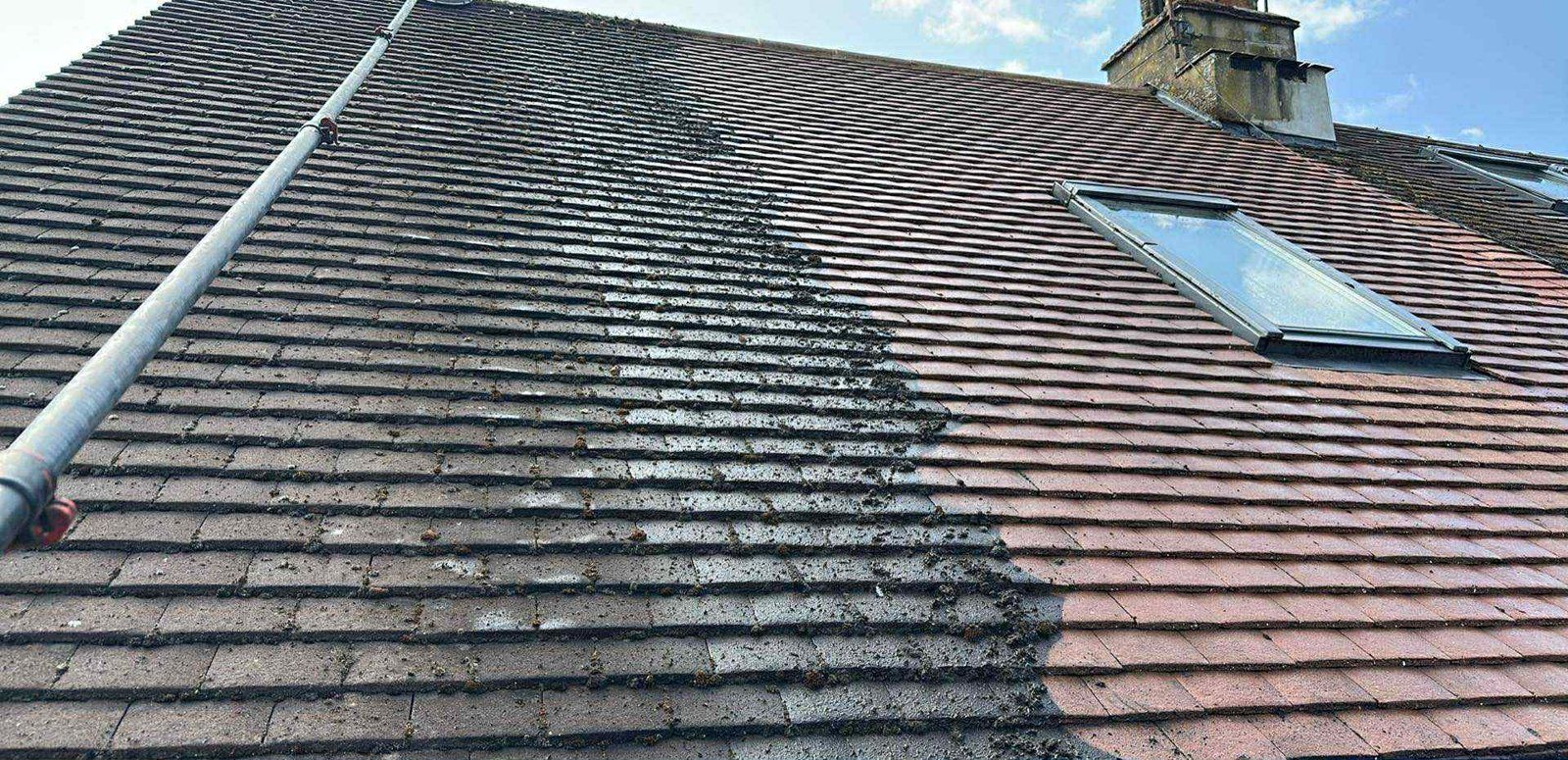 Clay tile roof with a roof window, half cleaned, dark mossy tiles on the left and clean red tiles on the right