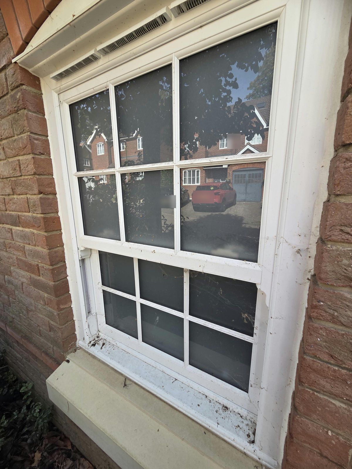 White uPVC Georgian-bar sash window with cobwebs, insects and dirt on the frame and sill