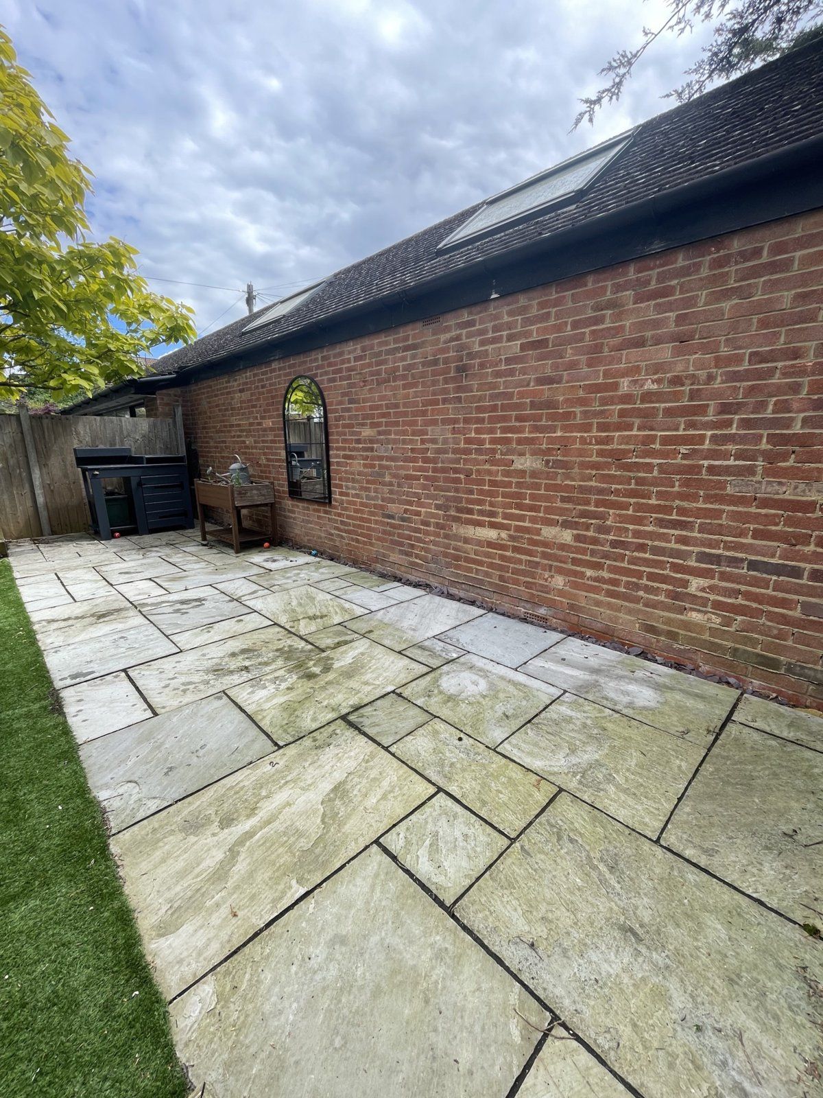 Before: grey sandstone patio streaked with green algae beside a brick wall