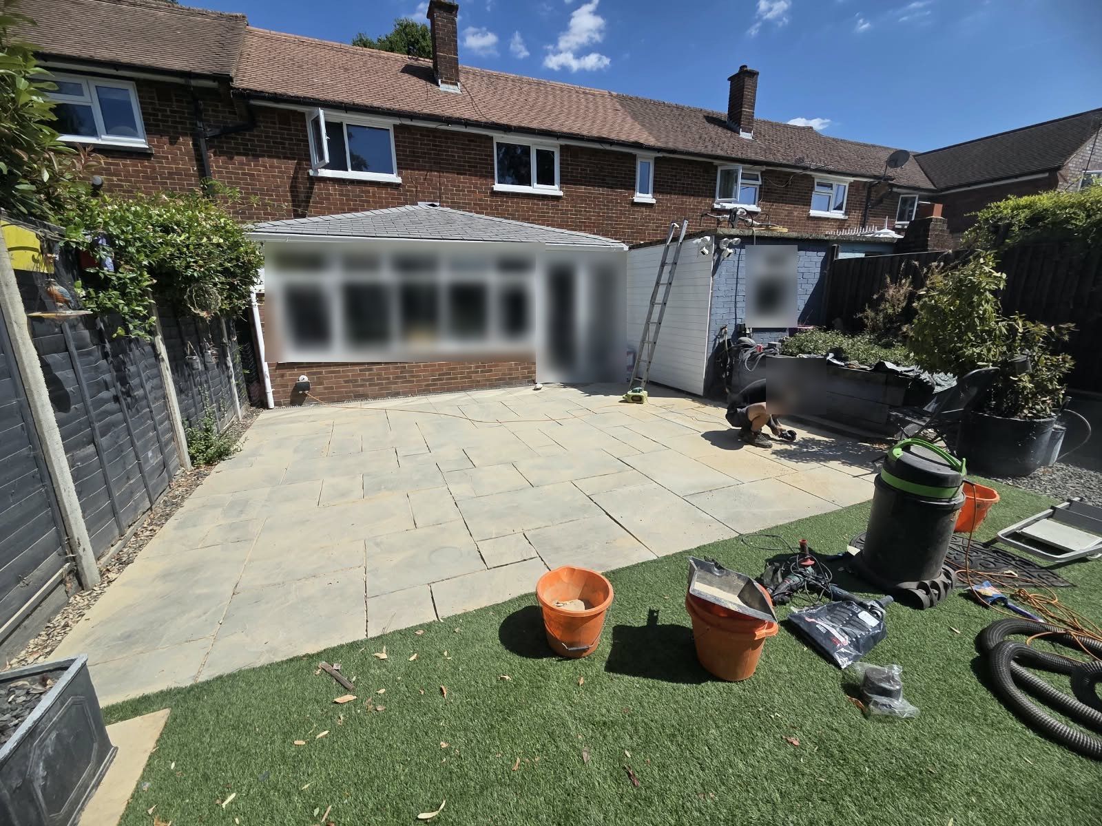 Large grey sandstone patio behind a terrace, part-way through the job, with buckets and tools on the lawn