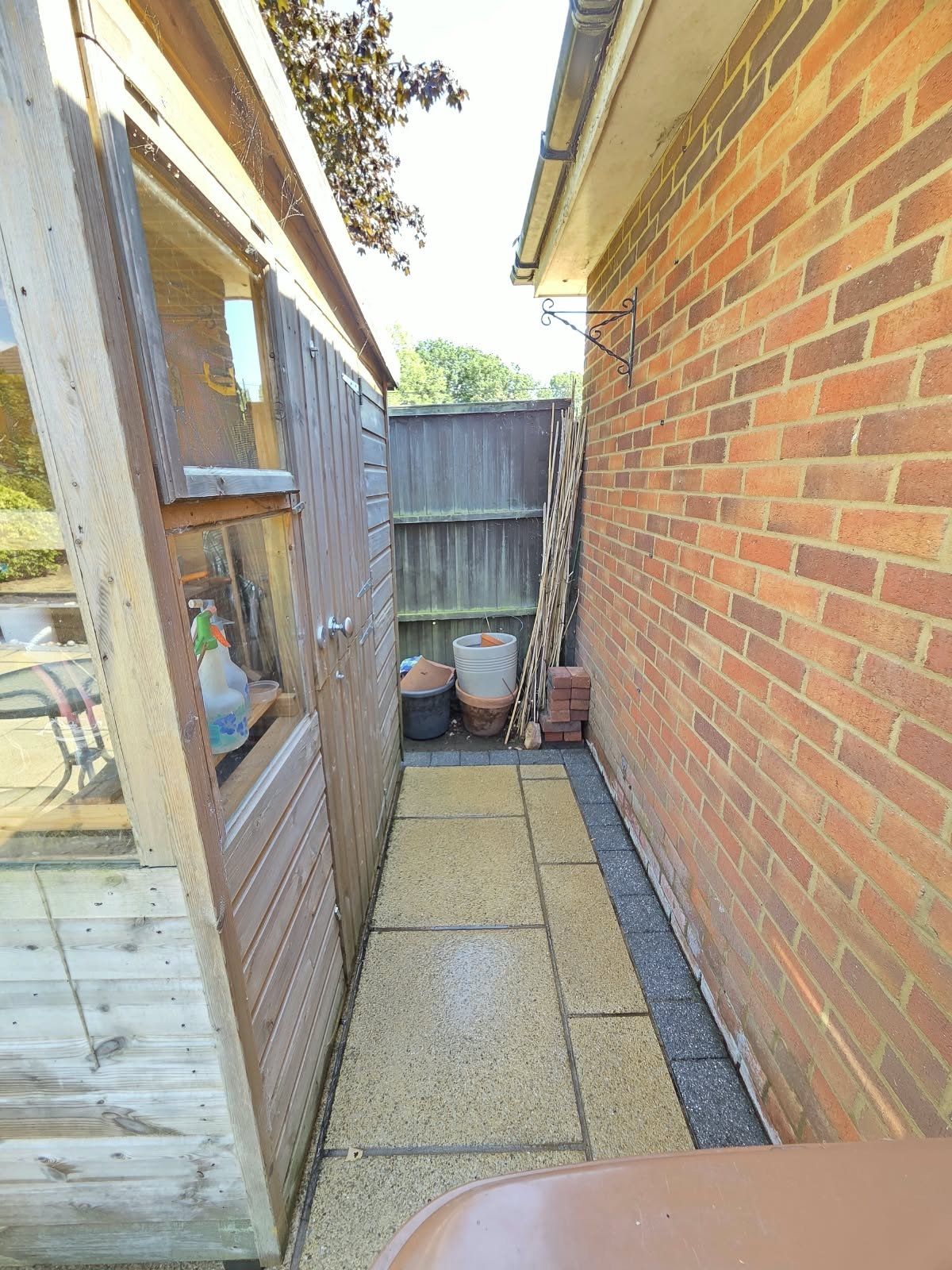 The same side path seen from further back, cleaned to buff slabs, still wet, with grey block edging