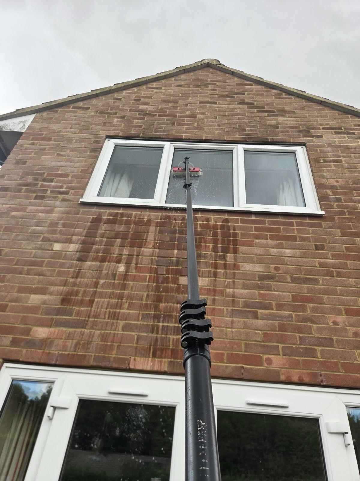Water-fed pole reaching a first-floor gable window, water running down the glass and brickwork