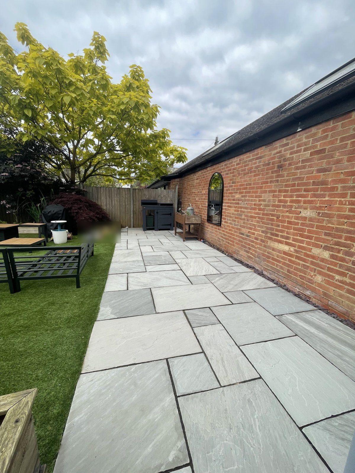 After: the same grey sandstone patio clean, beside artificial grass