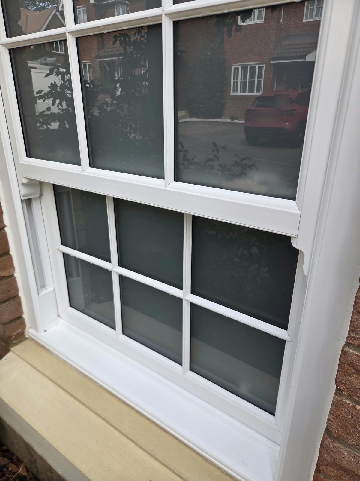 The same sash window after cleaning, frame, glazing bars and sill bright white with droplets on the bars