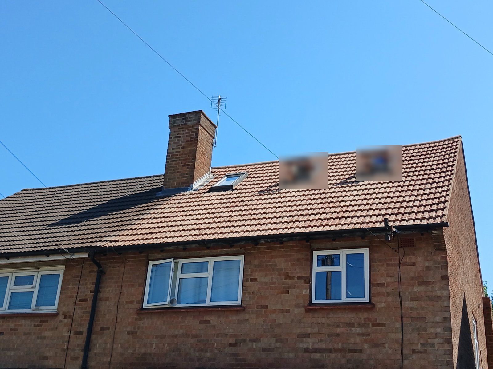 Front roof of the same house cleaned, bright tiles beside the neighbour's darker half, with three roof windows and a chimney