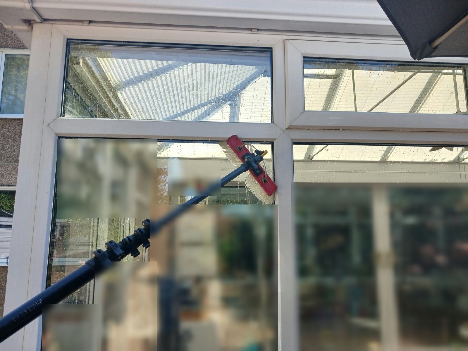 Water-fed pole brush cleaning conservatory glass and frames, with water running down the pane