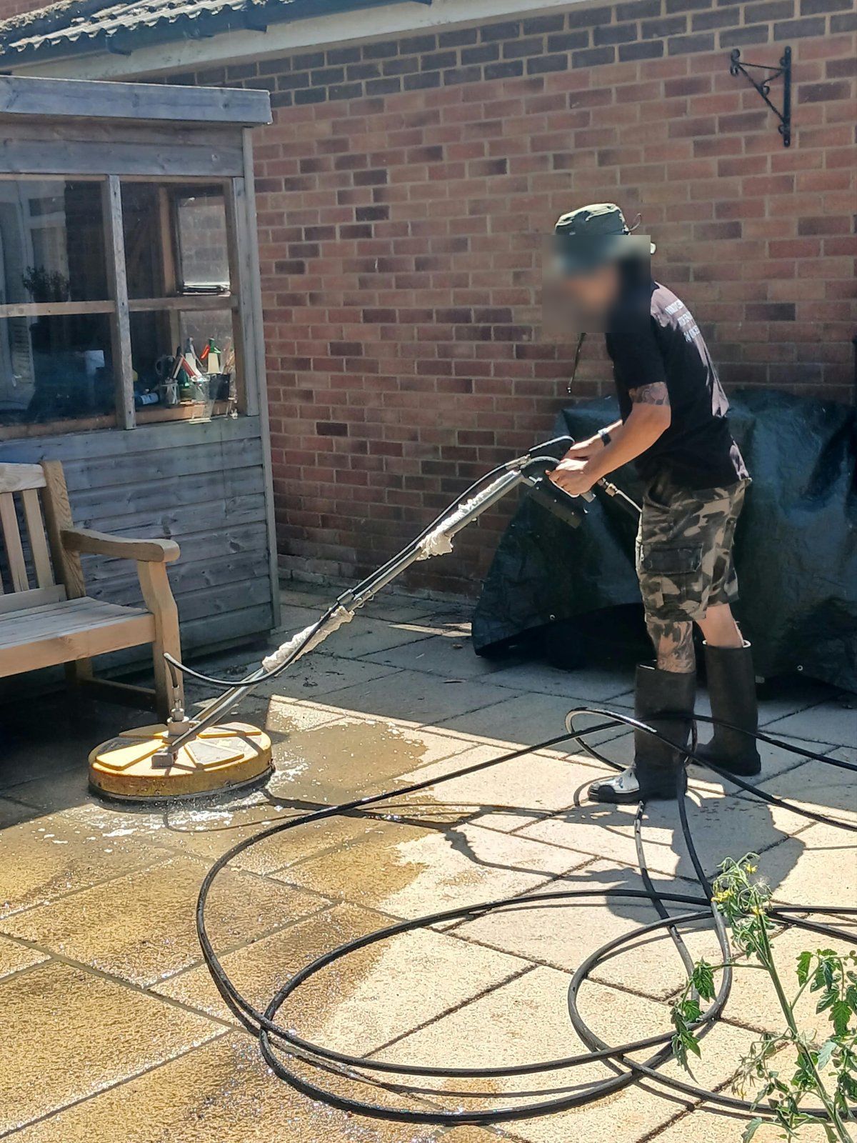 Rotary surface cleaner on buff concrete patio slabs, with the wet cleaned area beside it