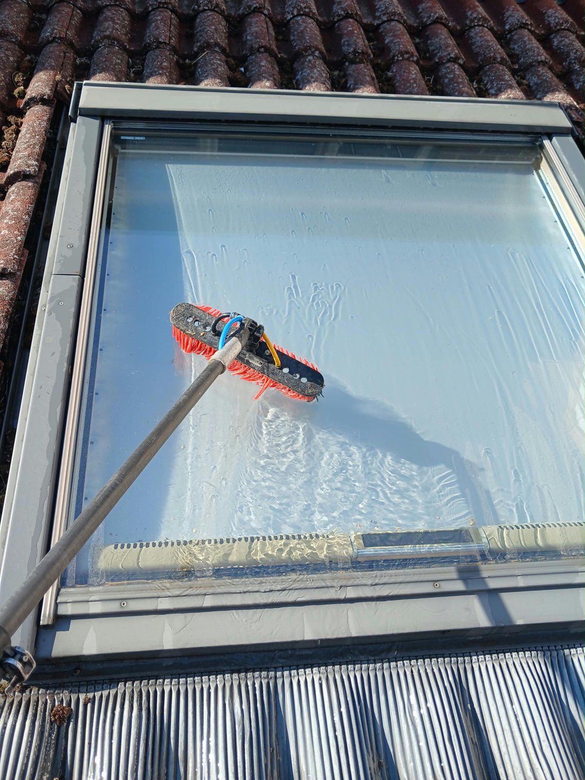 Brush on a water-fed pole cleaning a roof window set in clay tiles