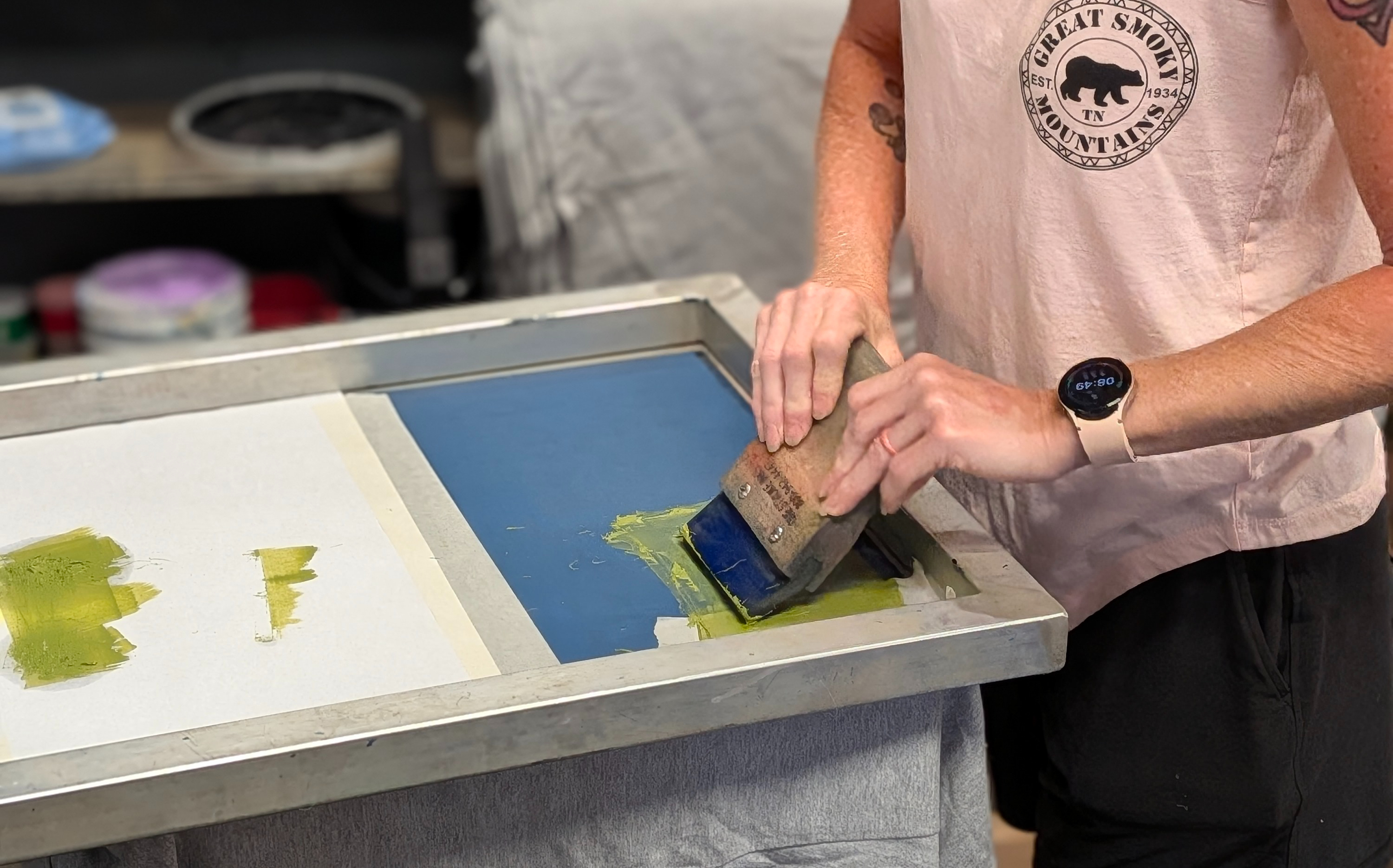 Screen printing press mid-print with visibly thick glow-in-the-dark ink being applied through the screen Screen printing press mid-print with visibly thick glow-in-the-dark ink being applied through the screen