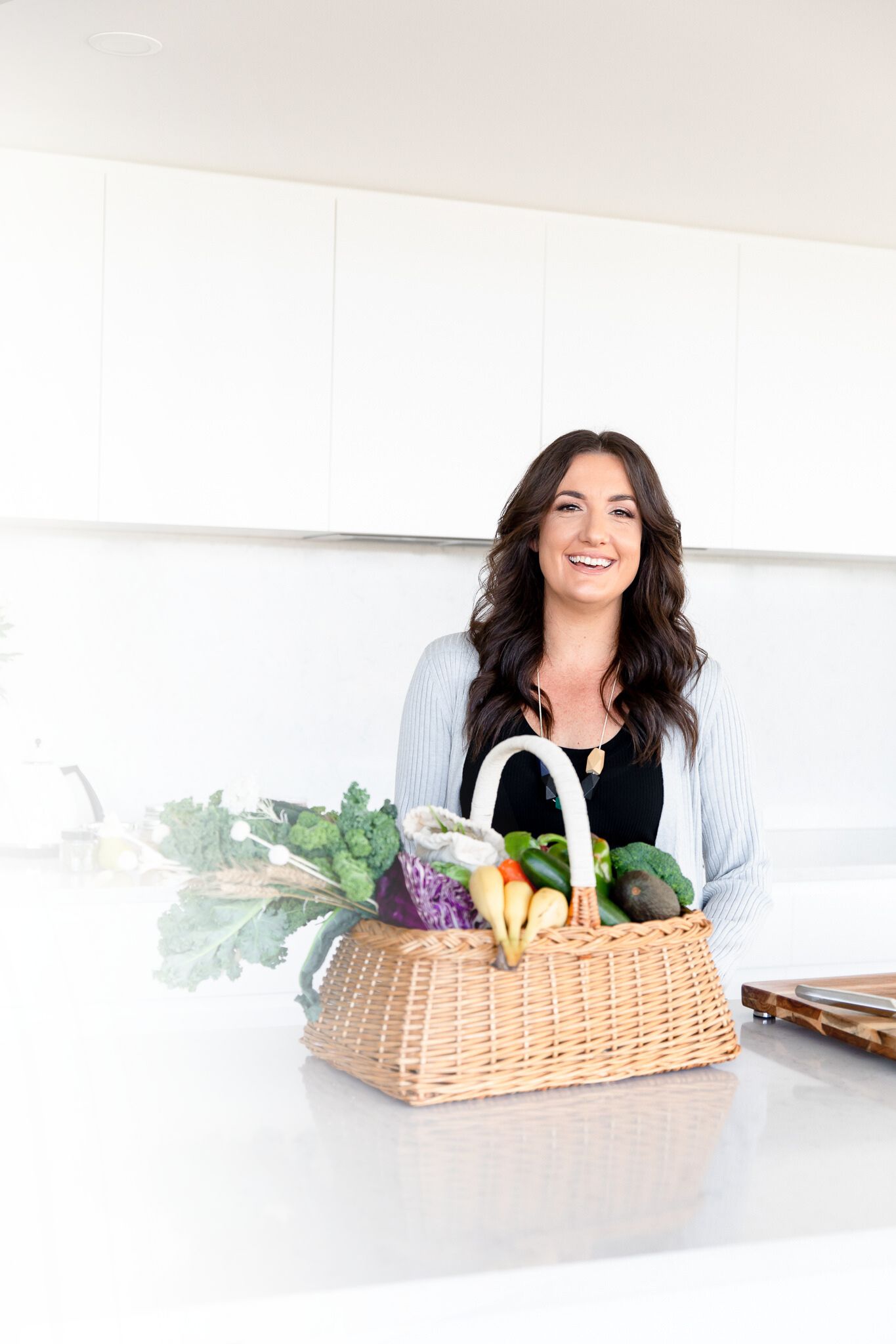 Melanie Lansdown in kitchen with basket of fresh fruit and vegetables — whole food approach to women’s hormone and energy support