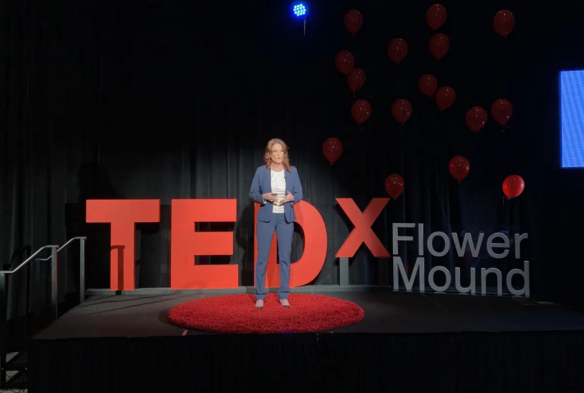 Tanya speaking on the TEDxFlowerMound stage, seen from the back of the room