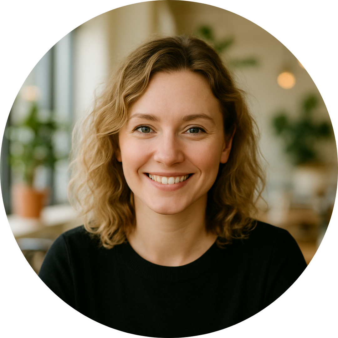 Uśmiechnięta kobieta z kręconymi blond włosami w czarnej bluzce, siedząca w jasnym wnętrzu z roślinami – zdjęcie profilowe eksperta lub mentorki biznesu.