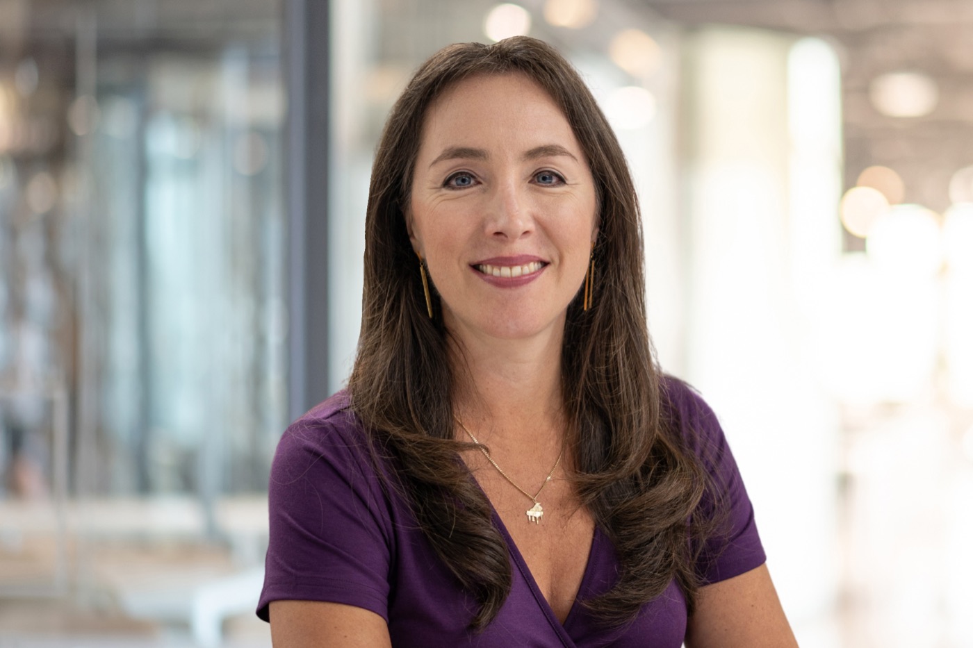 Dr. Fabiana Claure smiling to camera in a purple top, in a bright modern space