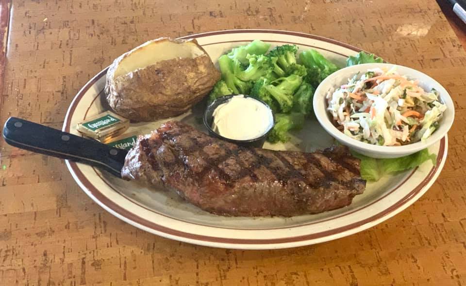 A steak dinner plate with broccoli, coleslaw, and baked potato