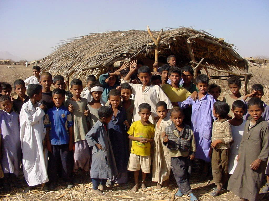 A crowd gathered in front of a stick-and-thatch shelter in northeast Sudan