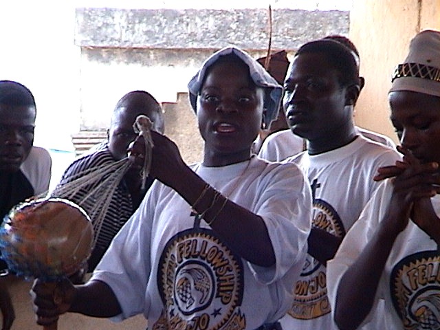 Believers in Sierra Leone mid-worship, singing together against a bare plaster wall