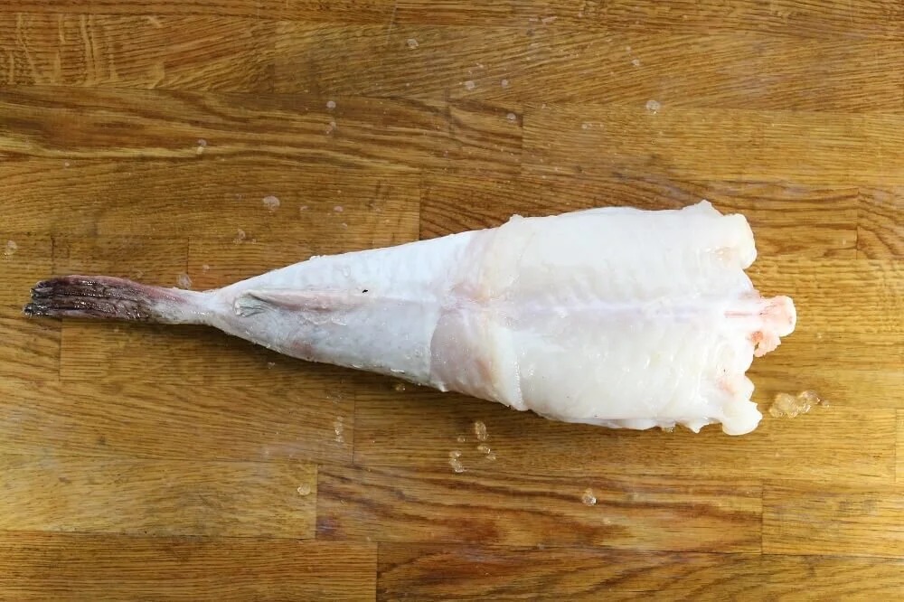 Queue de lotte fraîchement parée et prête à cuire sur un plan de travail en bois, un produit phare de l'arrivage quotidien du secteur marée à Rungis, France.