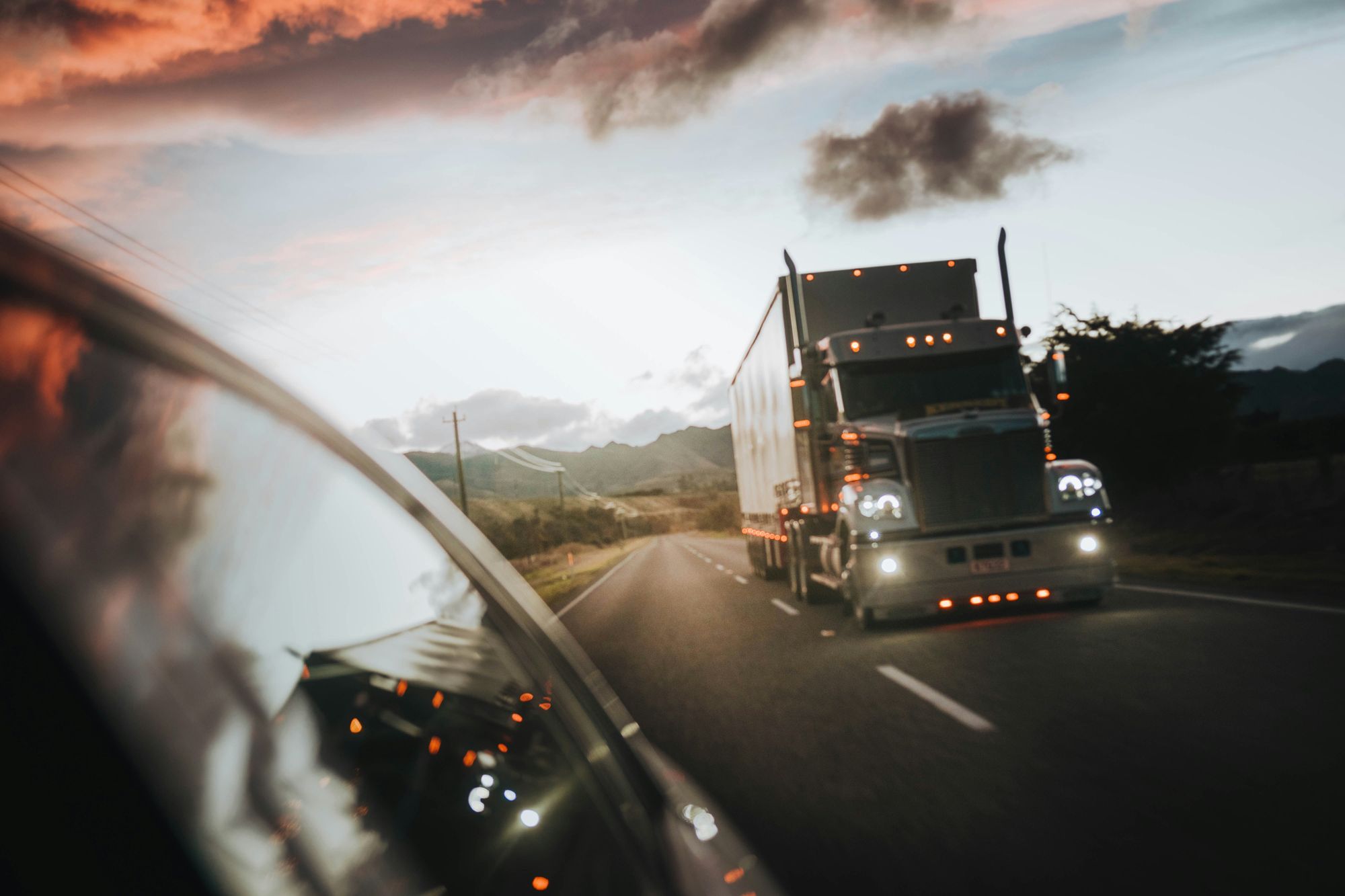 Semi truck with lights on driving a two-lane highway at dusk