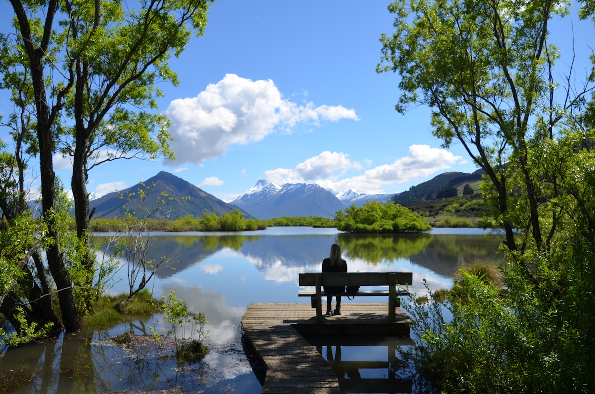 A person sitting by a lake at the foot of the mountains