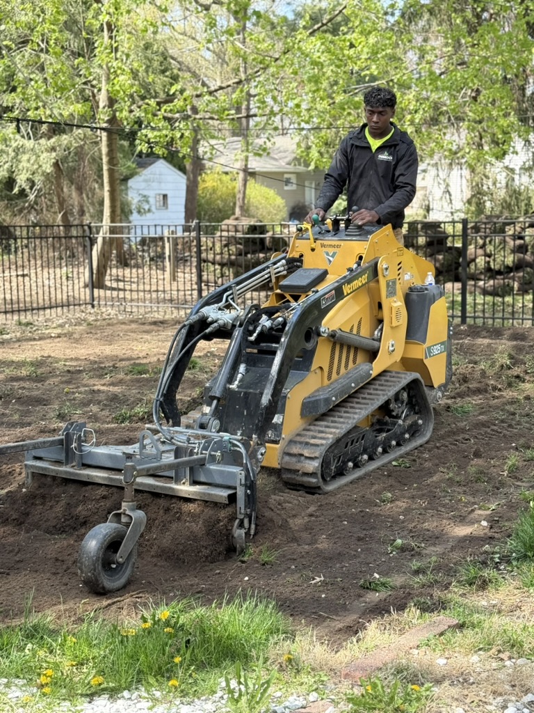 Crew member grading soil with a compact loader
