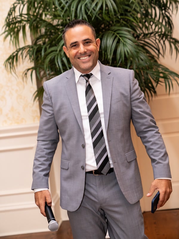 Chris Abazis smiling with a microphone while emceeing an event