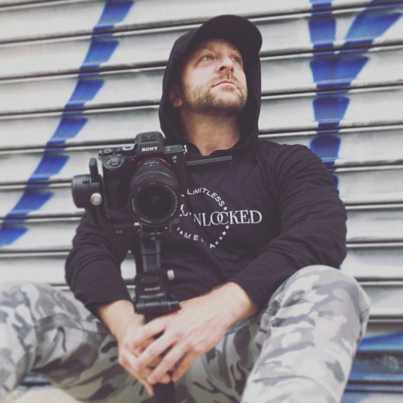 Jon sitting against a graffiti wall with a camera on a gimbal