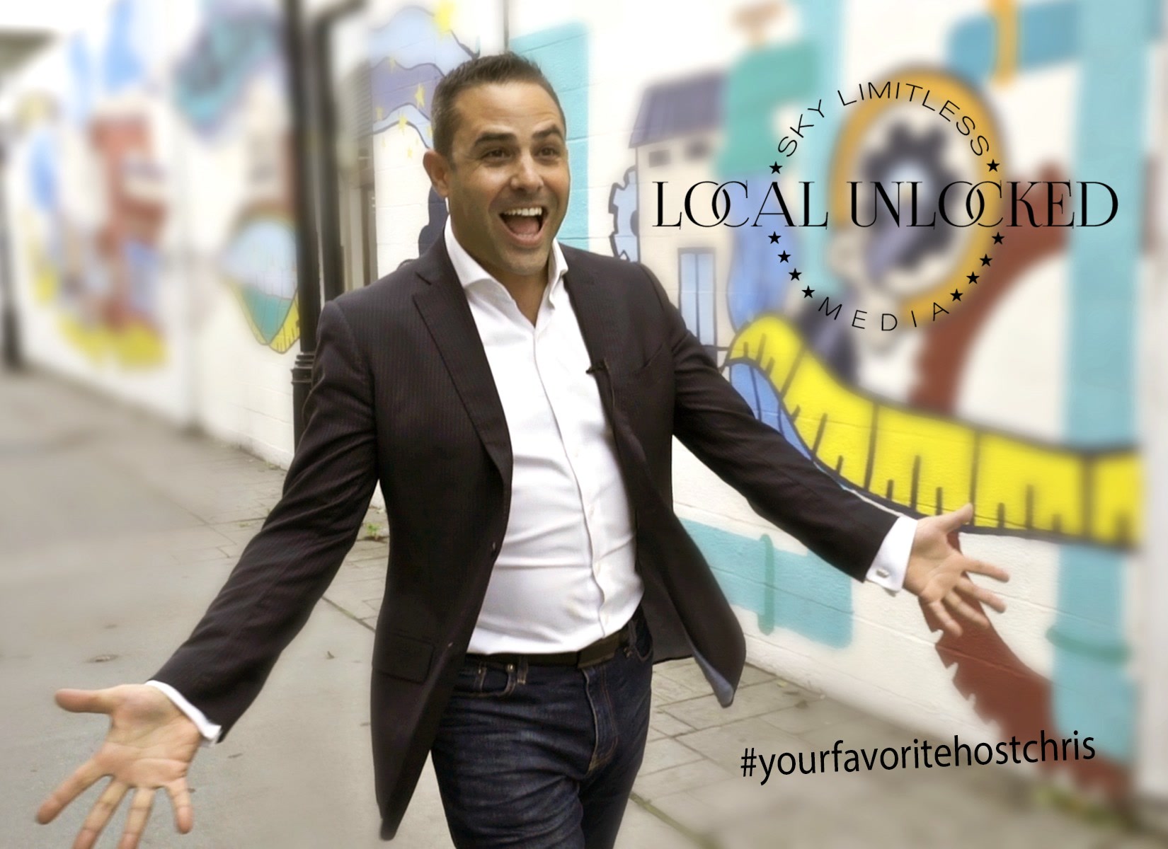 Chris Abazis, host of Local Unlocked, arms wide in front of a colorful mural