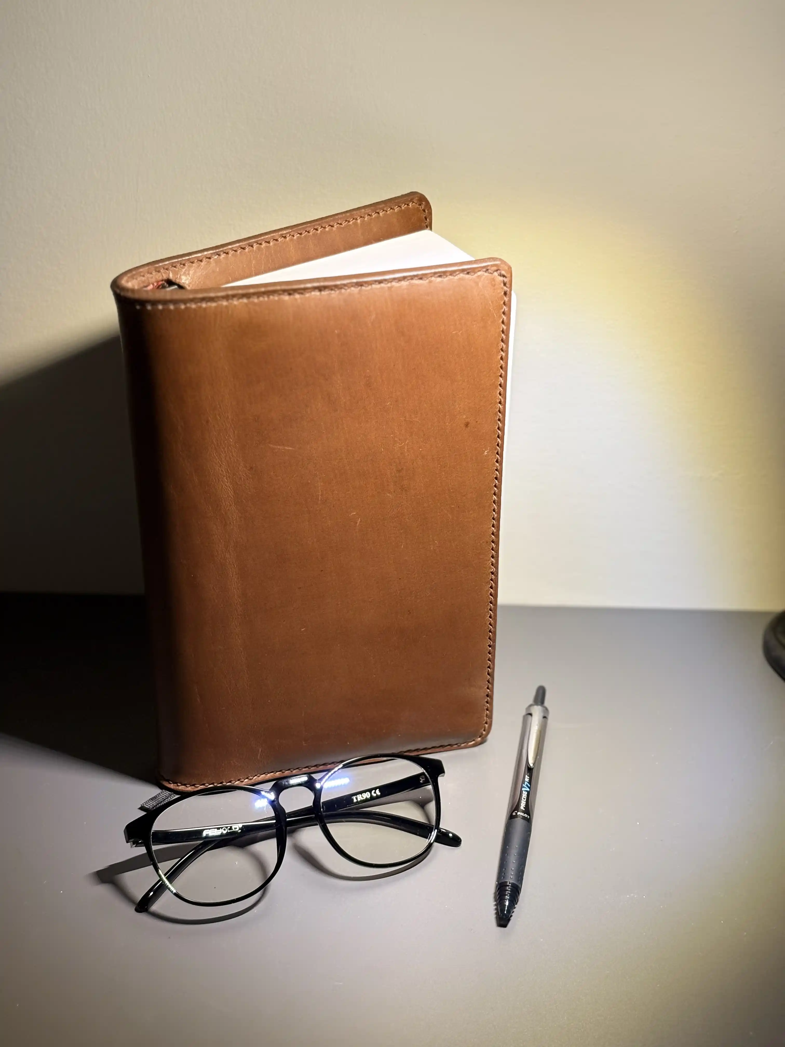 a pair of glasses, a pen, and a brown leather book