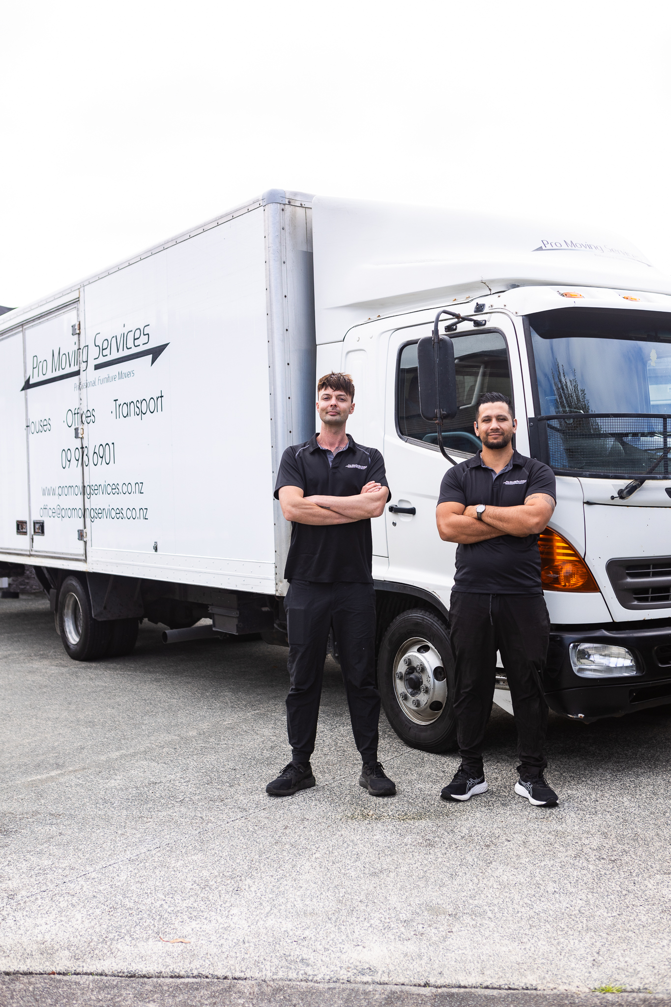Two professional movers from Pro Moving Services, wearing black tank tops and silver chains, smiling and representing the company's commitment to reliable moving services in Auckland.