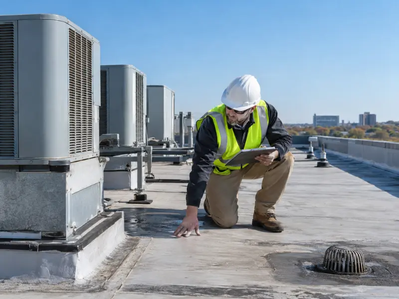 Inspector examining rooftop HVAC units and roof condition during commercial property inspection.