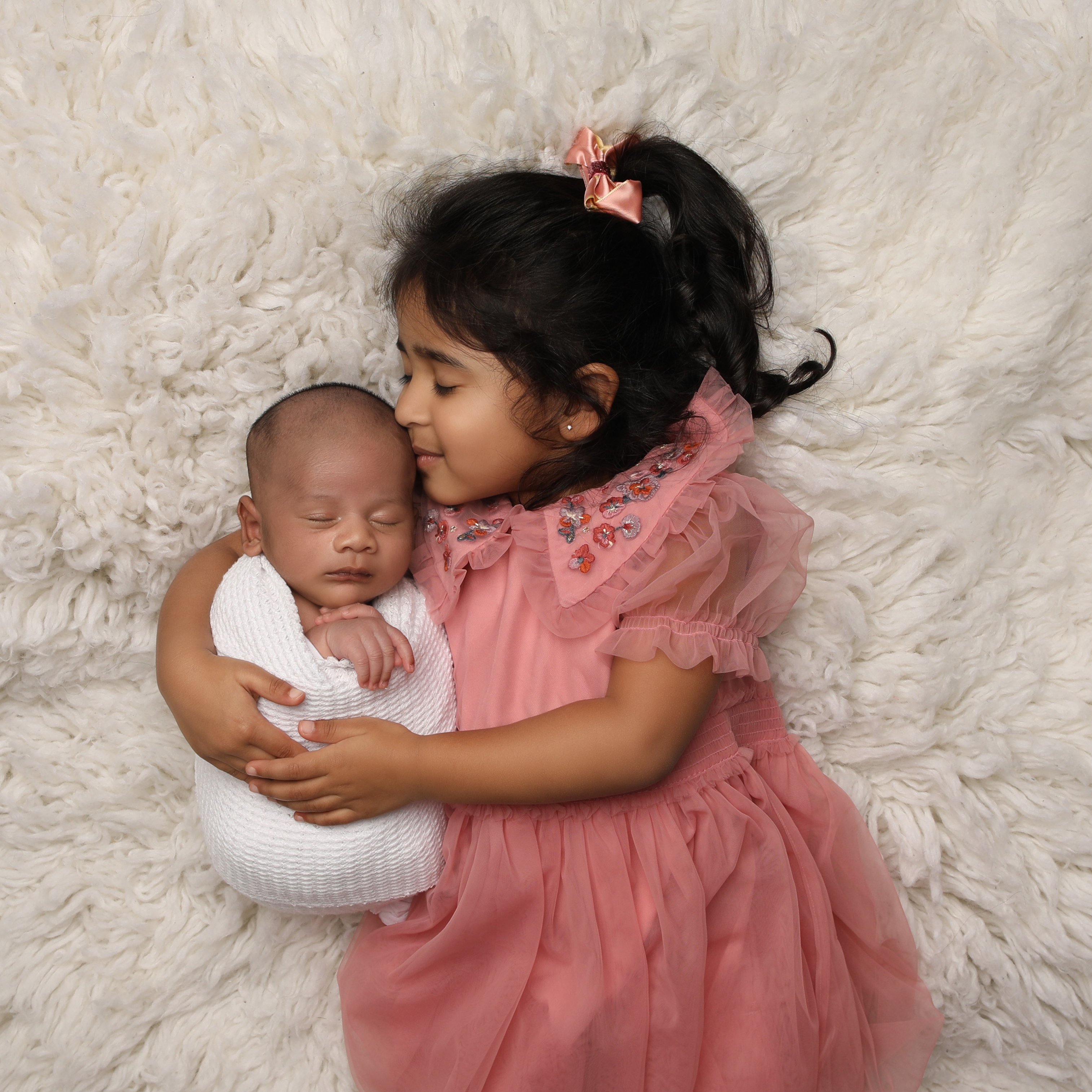 Older sister with baby sibling laying on blanket Professional baby photos taken by baby art Manchester