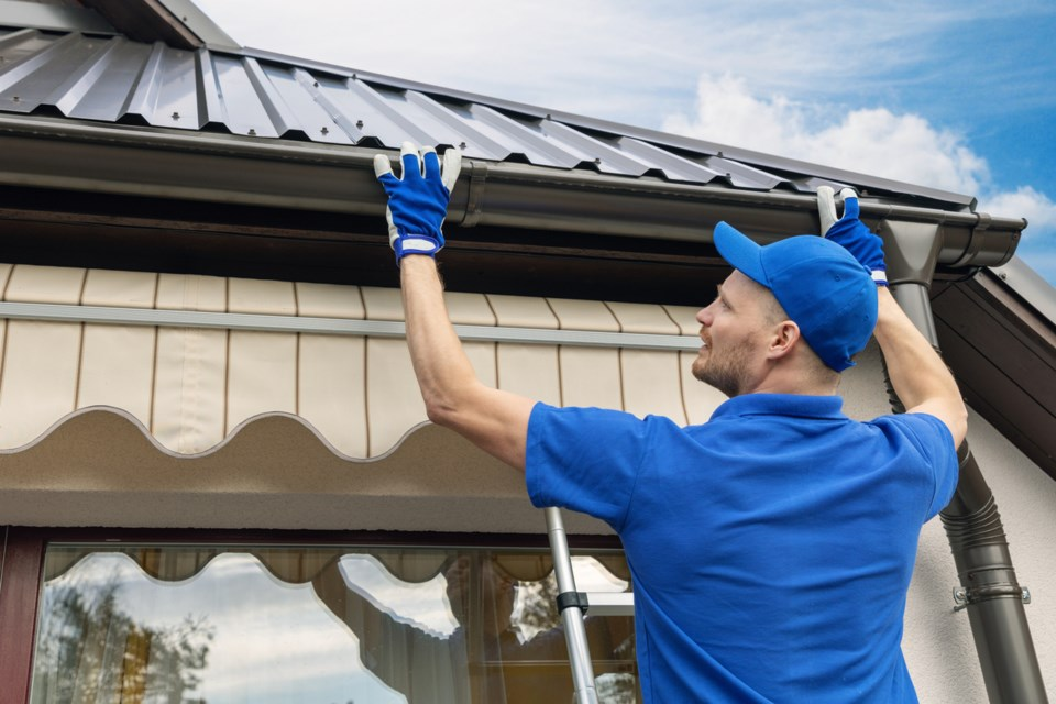 Worker installing gutters on a home roof Worker installing gutters on a home roof