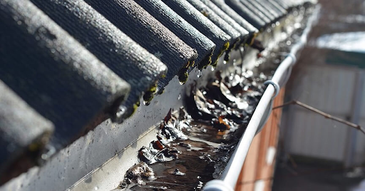 Clogged gutter filled with wet leaves and debris causing water overflow after winter