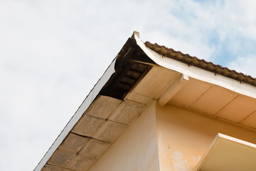 Damaged and rotting fascia board on a house roofline with peeling white paint.