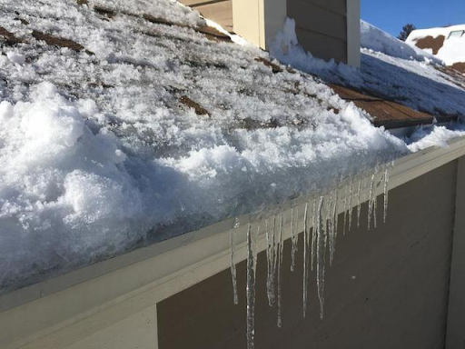 Ice dam formed on a residential roof edge with thick snow accumulation and icicles hanging from the gutter.