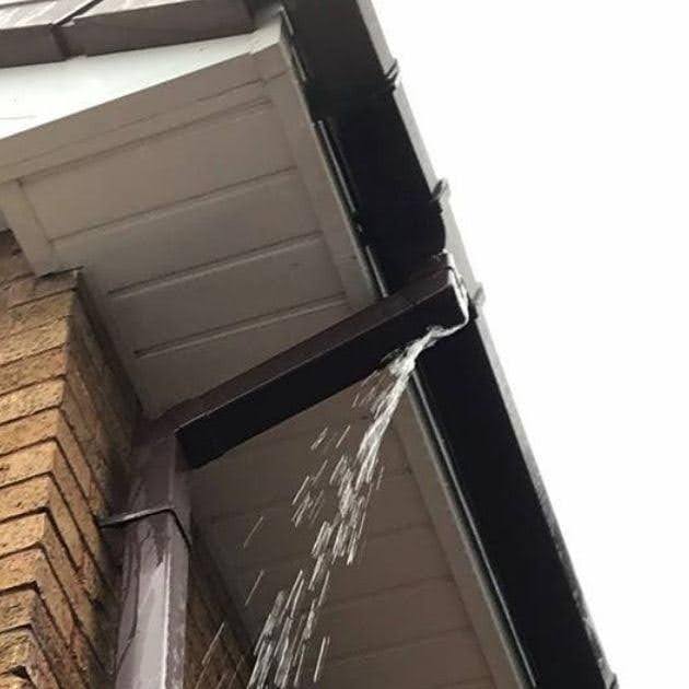   Water overflowing from a clogged roof gutter and spilling over the edge near a downspout.