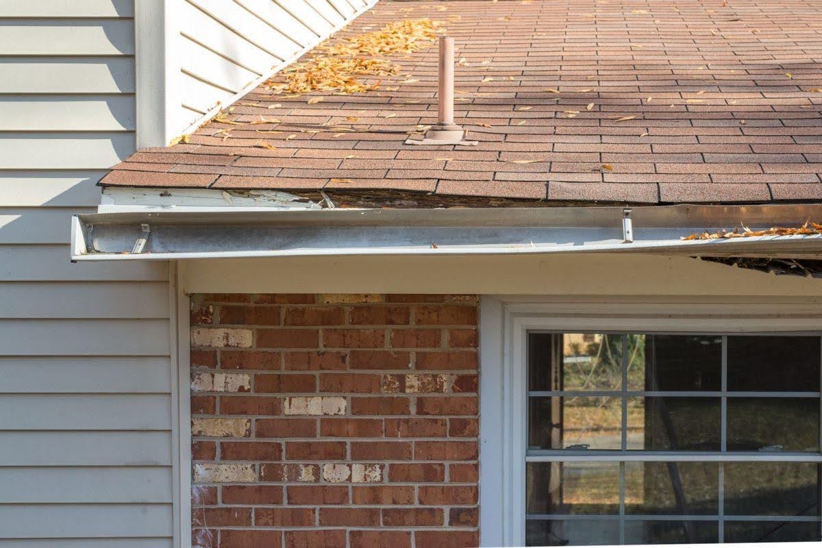 Damaged and sagging roof gutter pulling away from the fascia beneath a shingled roof.