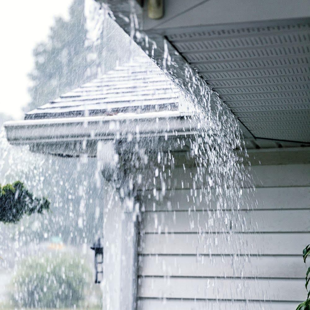 Rainwater pouring over the edge of a roof gutter due to a blocked or clogged downspout.