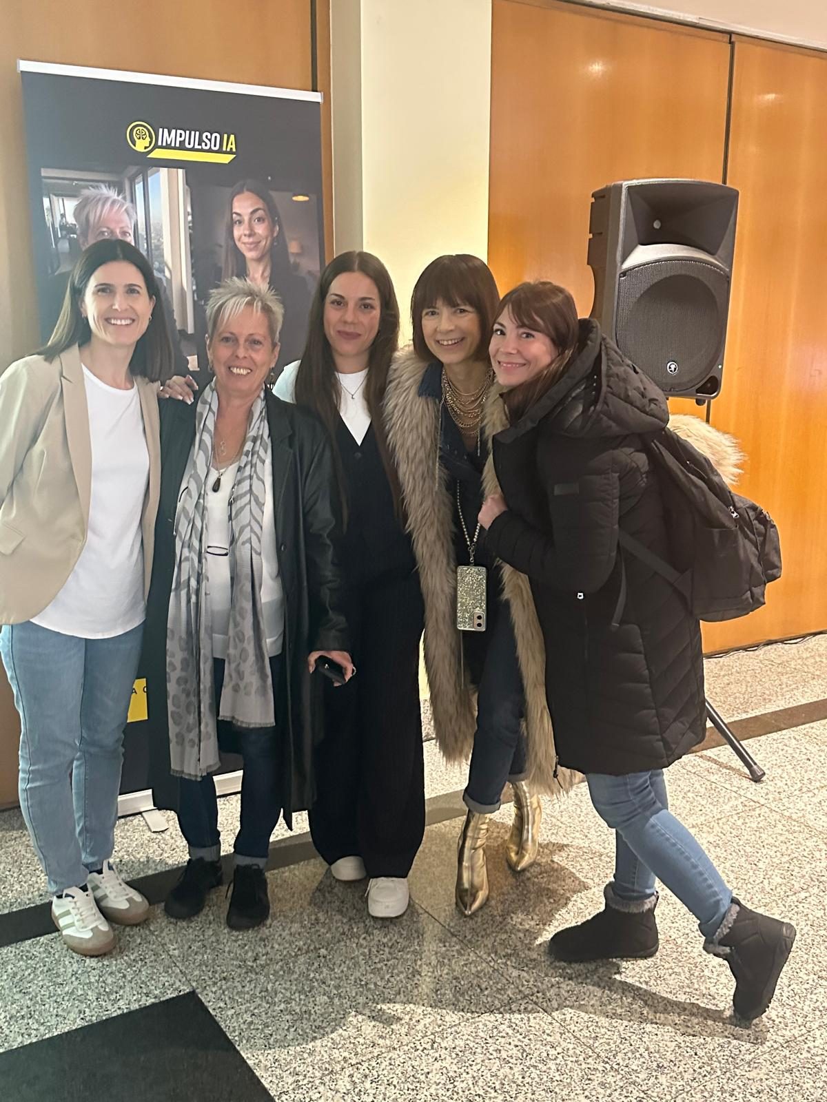 Las fundadoras con alumnas junto al cartel de Impulso IA