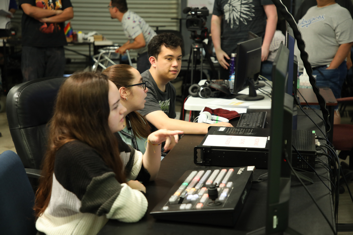 Students collaborating with cameras, scripts, sound equipment, and video editing tools during a hands-on creative production class.