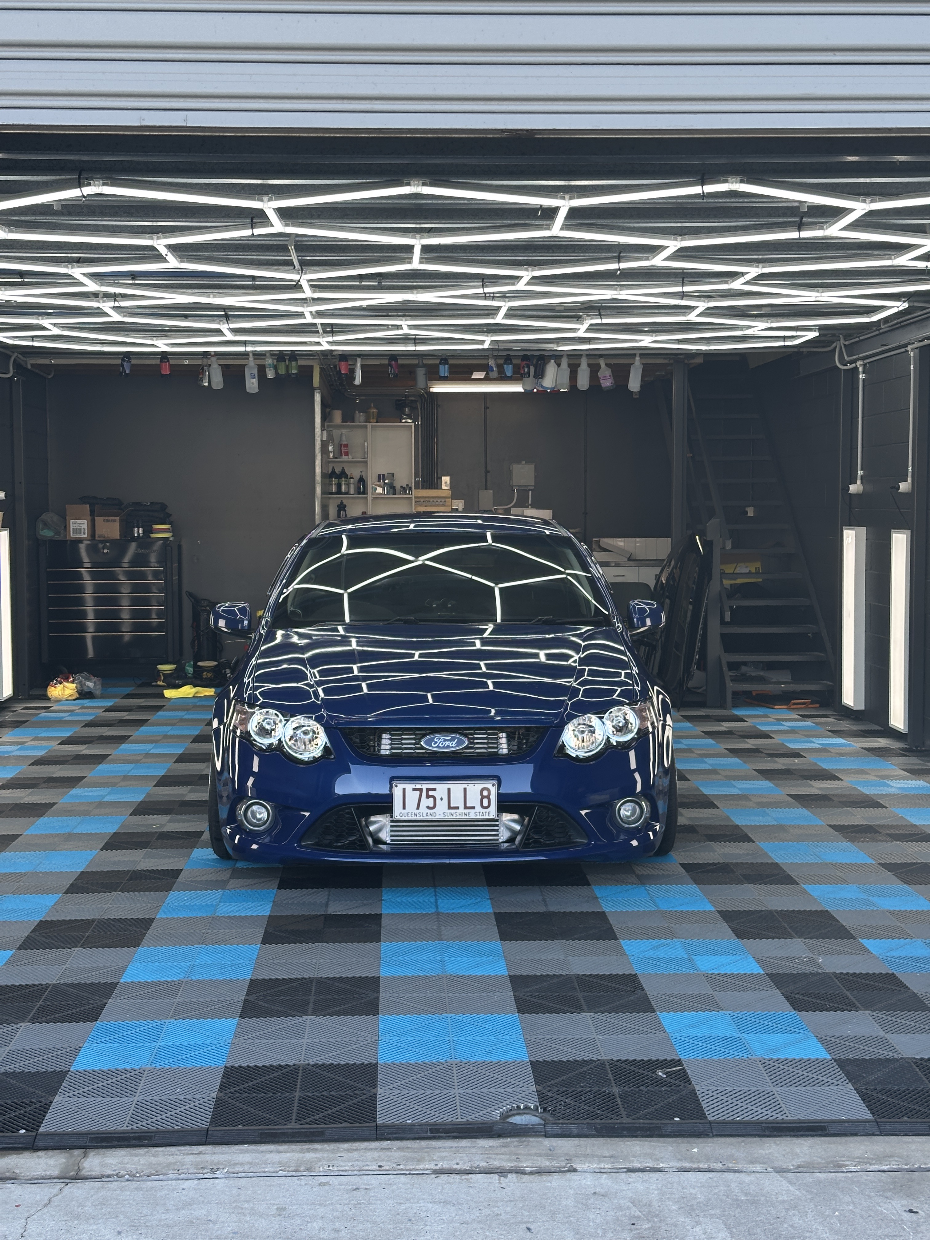 A blue sedan detailed in a workshop under overhead lighting