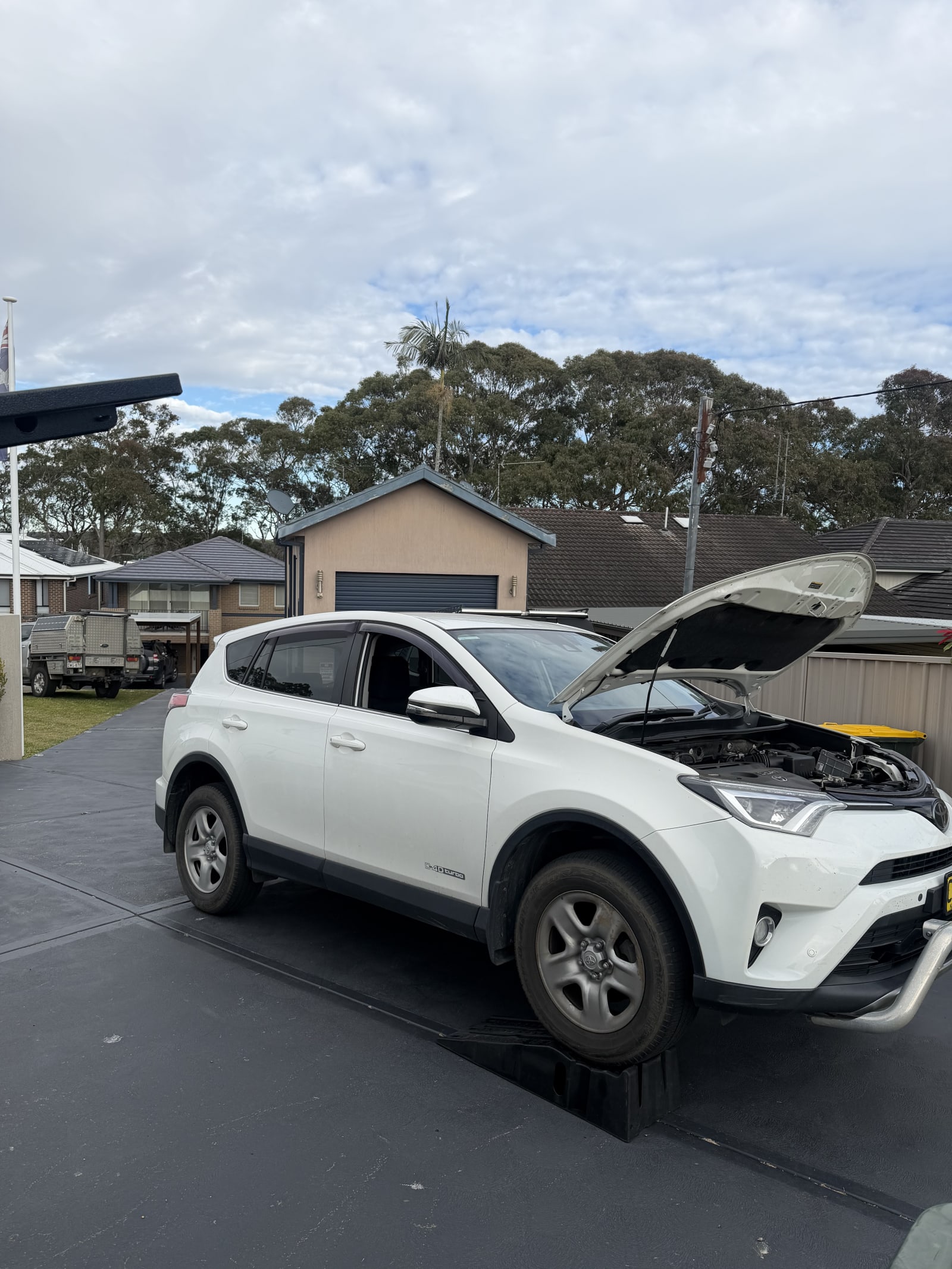 Toyota RAV4 on ramps in a driveway with the bonnet up, mid service