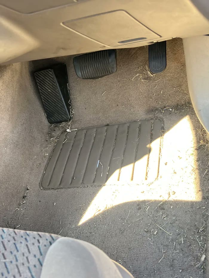 Driver footwell carpet covered in dirt and debris before detailing
