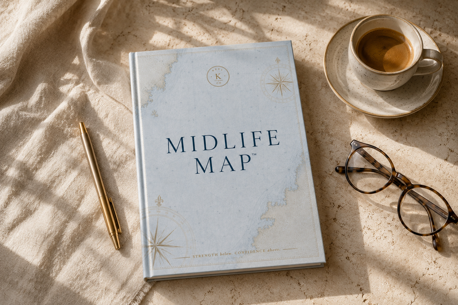 The Midlife Map workbook on linen beside a brass pen, espresso, and reading glasses in morning light
