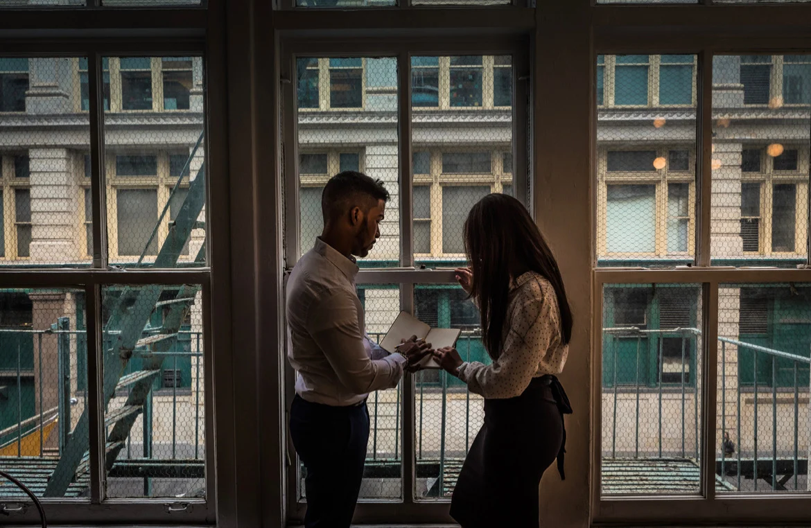 Ralph and a woman looking at a notebook together by a tall window