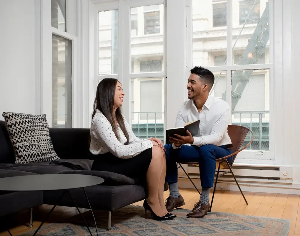 Ralph holding a notebook, in conversation with a client by a window