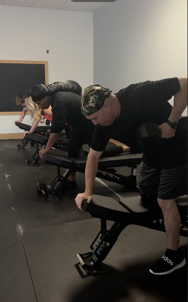 Members performing dumbbell rows at Portion Fitness